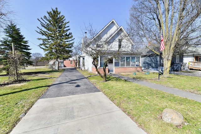 view of front facade with brick siding, a front yard, and a sunroom