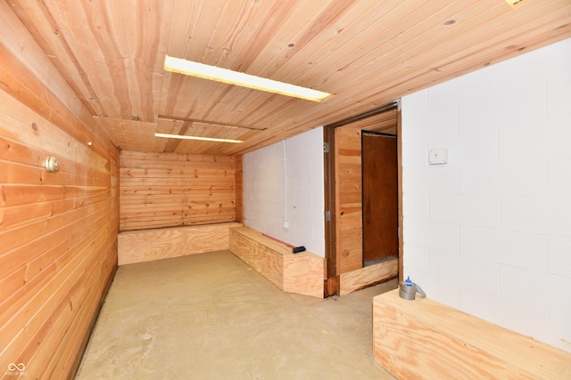 unfurnished room with concrete block wall, wooden ceiling, concrete flooring, and wood walls