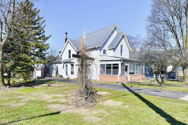 view of front of house with driveway, a front yard, a sunroom, brick siding, and a chimney