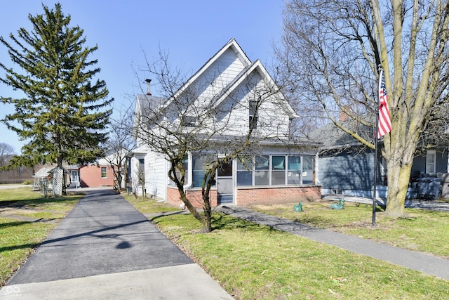 view of front of home with a front yard, brick siding, and a sunroom