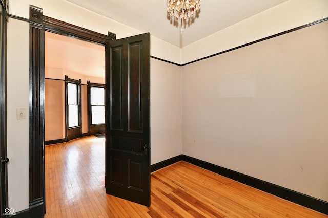 empty room featuring an inviting chandelier, a barn door, baseboards, and light wood finished floors