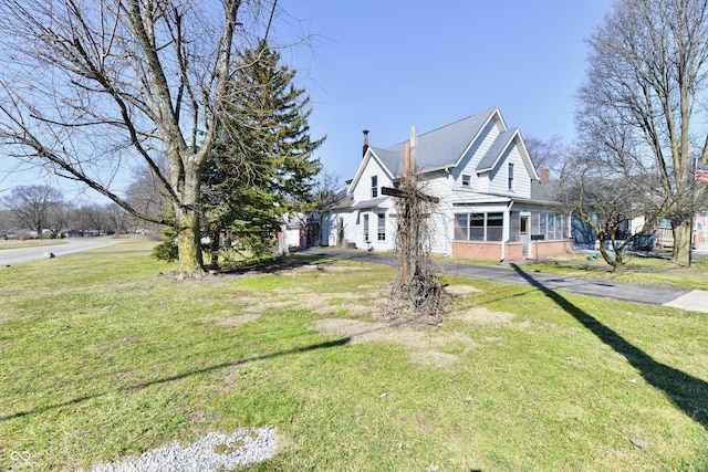 view of front of home with aphalt driveway, brick siding, a chimney, and a front lawn