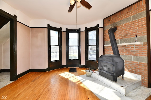 unfurnished living room with ceiling fan, a wood stove, baseboards, and hardwood / wood-style flooring