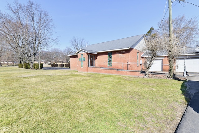 exterior space featuring a garage, brick siding, a lawn, and fence