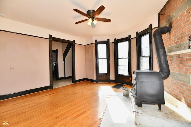 interior space featuring wood finished floors, brick wall, baseboards, ceiling fan, and a wood stove