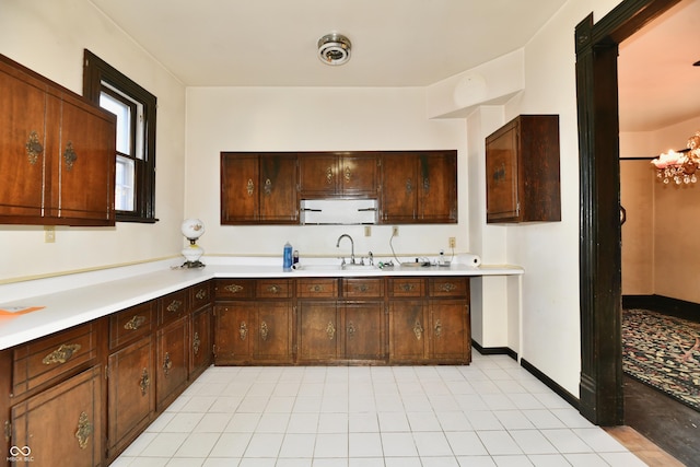 kitchen with a sink, baseboards, dark brown cabinetry, and light countertops