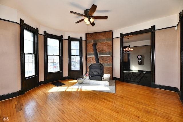 unfurnished room with a ceiling fan, a wood stove, a healthy amount of sunlight, and wood-type flooring