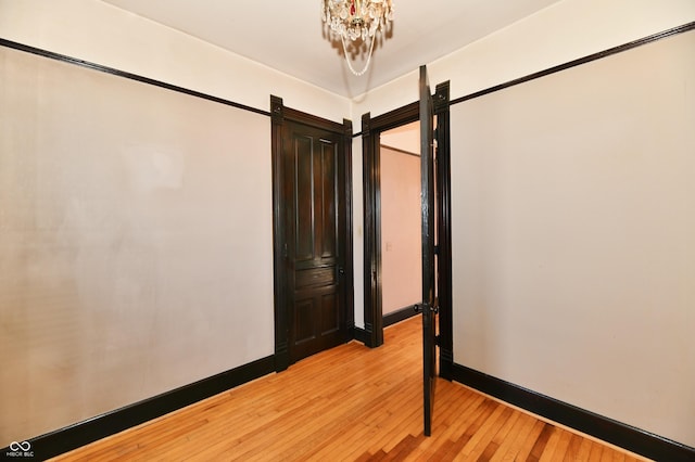 unfurnished room with a notable chandelier, light wood-style floors, and baseboards