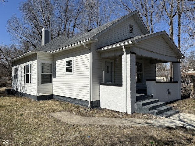 view of home's exterior featuring roof with shingles, a porch, and a chimney