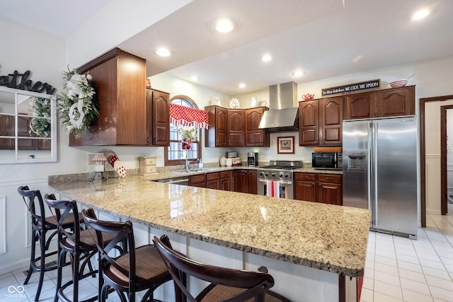 kitchen featuring wall chimney range hood, a kitchen bar, a peninsula, stainless steel appliances, and a sink