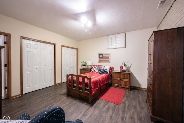 bedroom with visible vents, two closets, baseboards, and wood finished floors