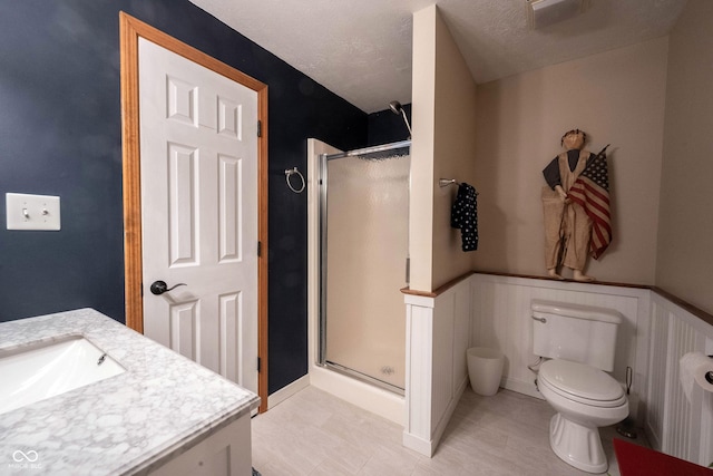 full bath featuring a wainscoted wall, a stall shower, toilet, and vanity