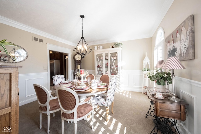 carpeted dining space with a wainscoted wall, a decorative wall, visible vents, and a chandelier