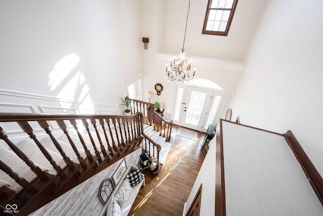 staircase featuring a notable chandelier, wood finished floors, and a towering ceiling