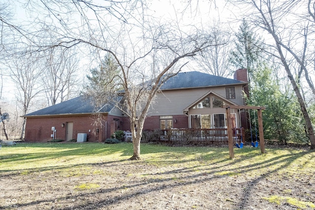 rear view of property with brick siding, a wooden deck, a lawn, and a chimney