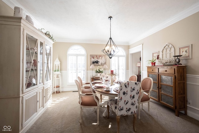 dining area featuring carpet floors, an inviting chandelier, wainscoting, crown molding, and a decorative wall