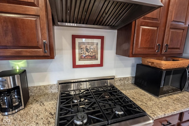 kitchen with light stone counters, range with gas stovetop, wall chimney exhaust hood, and black microwave