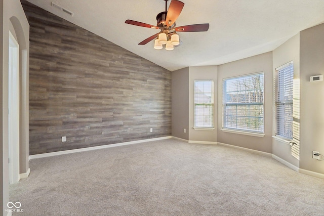 spare room with wooden walls, carpet, visible vents, vaulted ceiling, and an accent wall