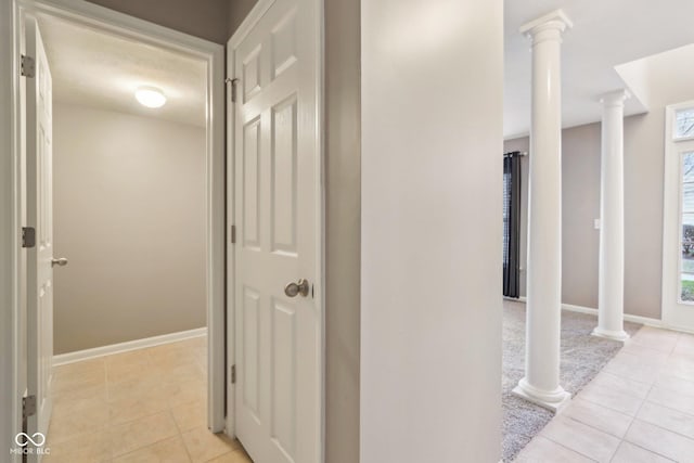 corridor with light tile patterned floors, baseboards, and decorative columns