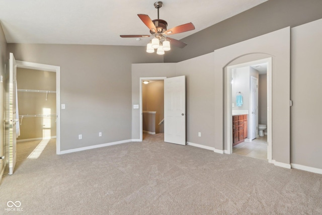 unfurnished bedroom with a walk in closet, light carpet, ensuite bathroom, a closet, and baseboards