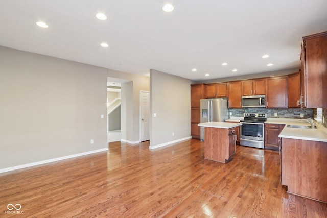 kitchen with a sink, backsplash, a kitchen island, appliances with stainless steel finishes, and light countertops