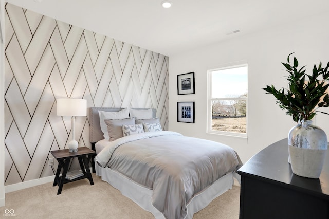 bedroom featuring an accent wall, light colored carpet, visible vents, and baseboards