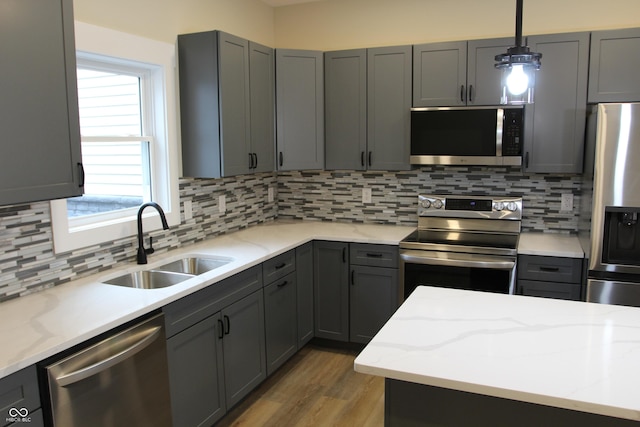 kitchen with gray cabinetry, a sink, tasteful backsplash, wood finished floors, and stainless steel appliances