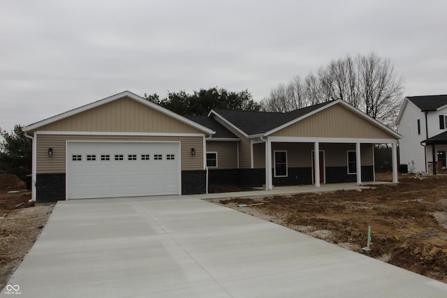 single story home with stone siding, an attached garage, covered porch, and driveway