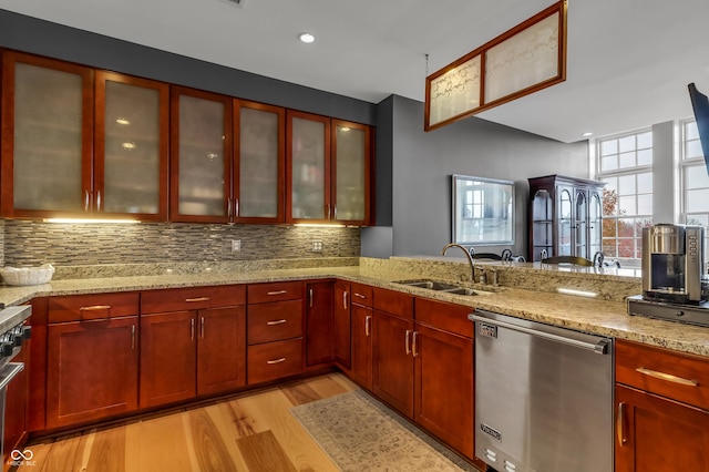 kitchen with light wood-style flooring, a sink, light stone counters, stainless steel dishwasher, and decorative backsplash