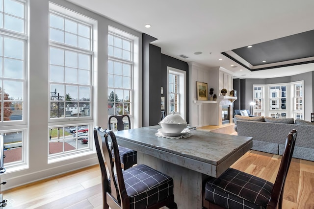 dining room with visible vents, a tray ceiling, recessed lighting, light wood-style flooring, and a glass covered fireplace