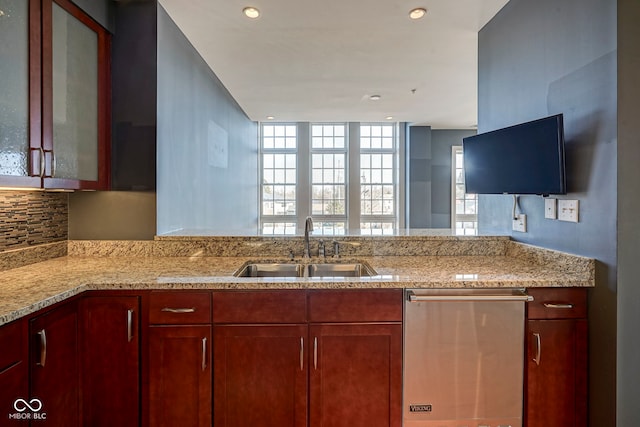 kitchen with backsplash, glass insert cabinets, light stone counters, stainless steel dishwasher, and a sink