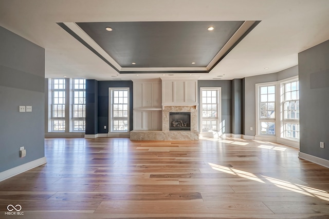 unfurnished living room featuring baseboards, recessed lighting, a fireplace, wood finished floors, and a raised ceiling