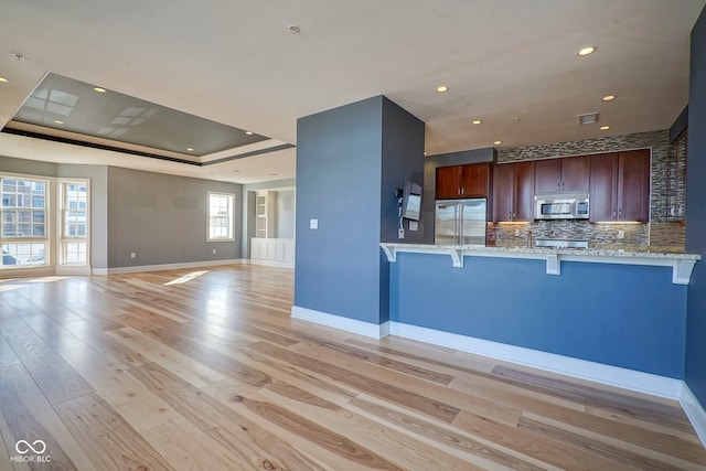 kitchen with light wood-type flooring, stainless steel appliances, a raised ceiling, and a breakfast bar area