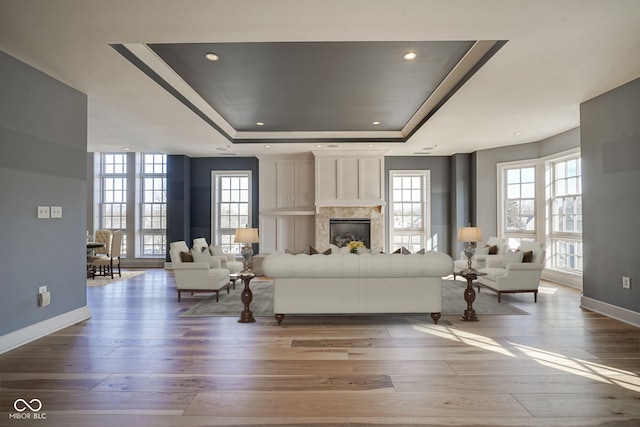 unfurnished living room with a glass covered fireplace, a tray ceiling, baseboards, and wood finished floors