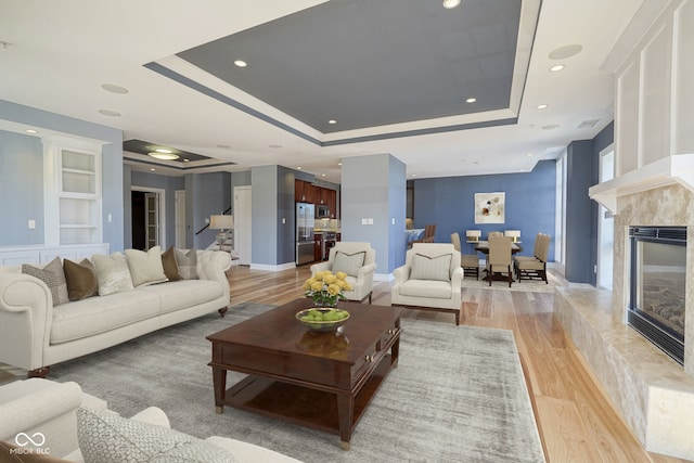 living room featuring a high end fireplace, built in shelves, light wood-type flooring, recessed lighting, and a raised ceiling