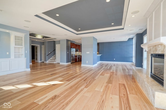 unfurnished living room featuring light wood finished floors, built in features, stairs, a fireplace, and a raised ceiling