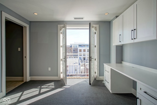 unfurnished office with baseboards, visible vents, dark colored carpet, and built in study area