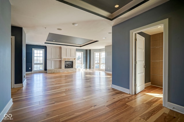 unfurnished living room featuring baseboards, a tray ceiling, a fireplace, recessed lighting, and light wood-style floors