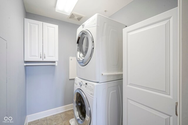 washroom featuring light tile patterned floors, baseboards, visible vents, stacked washing maching and dryer, and laundry area