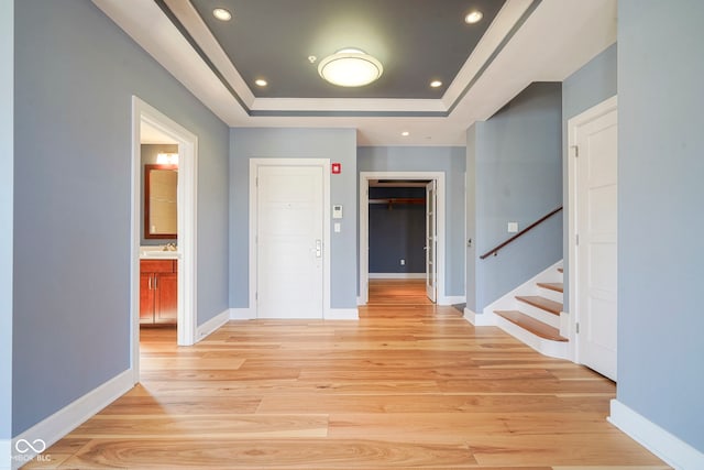 hallway with light wood-style flooring, baseboards, stairs, and a tray ceiling