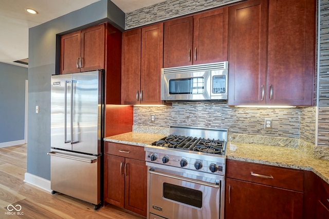 kitchen featuring light stone counters, high quality appliances, light wood-type flooring, and tasteful backsplash