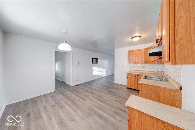 kitchen featuring light wood-style flooring, a sink, light countertops, under cabinet range hood, and backsplash