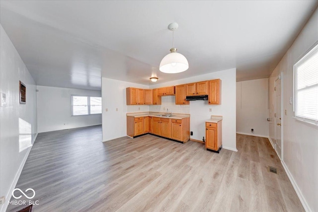 kitchen with visible vents, under cabinet range hood, decorative light fixtures, light wood-style flooring, and a sink