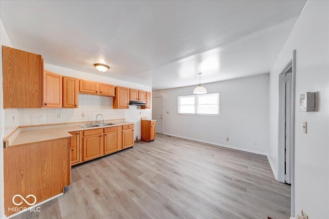 kitchen featuring baseboards, light wood-style flooring, a sink, decorative light fixtures, and tasteful backsplash