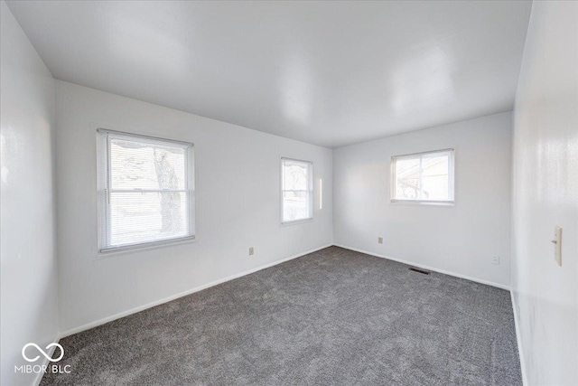 spare room with visible vents, baseboards, and dark carpet