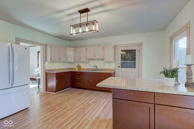 kitchen featuring pendant lighting, light stone counters, light wood-style flooring, freestanding refrigerator, and a sink