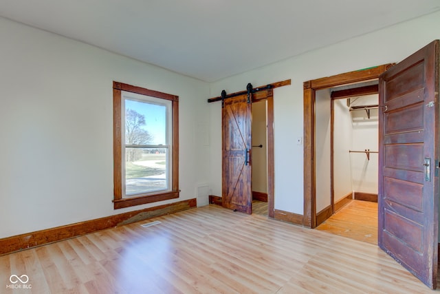 unfurnished bedroom with visible vents, baseboards, light wood-type flooring, and a barn door