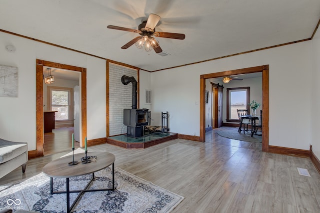 living area with visible vents, ornamental molding, a wood stove, and wood finished floors