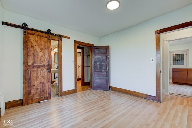 unfurnished room featuring a barn door, light wood-style floors, and baseboards