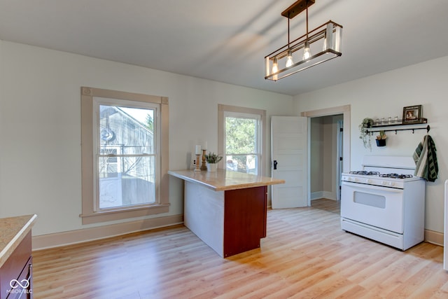 kitchen featuring a peninsula, light wood-style flooring, light countertops, and white gas range